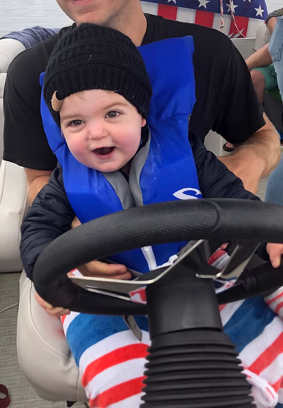 Child in life jacket steering a boat.
